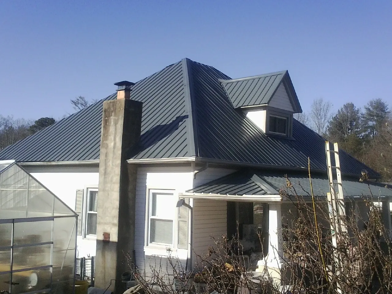 Dark blue standing seam metal roof on a white farmhouse with dormer — Slate & Tile Roof Repair by Roofing Brothers in Grandville