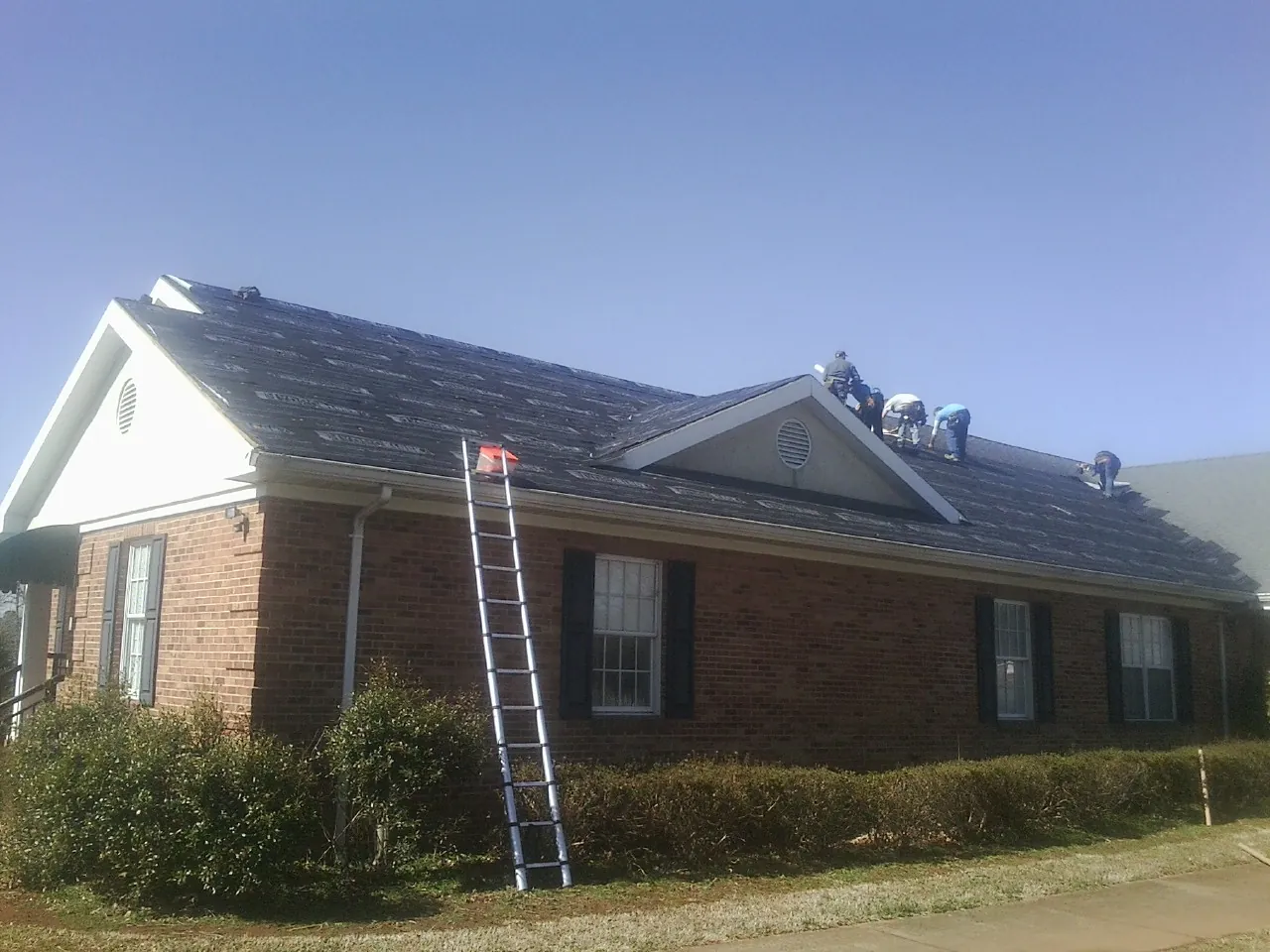 Crew tearing shingles off a brick ranch roof with a ladder set — Emergency Roof Repair work by our crew in Grandville