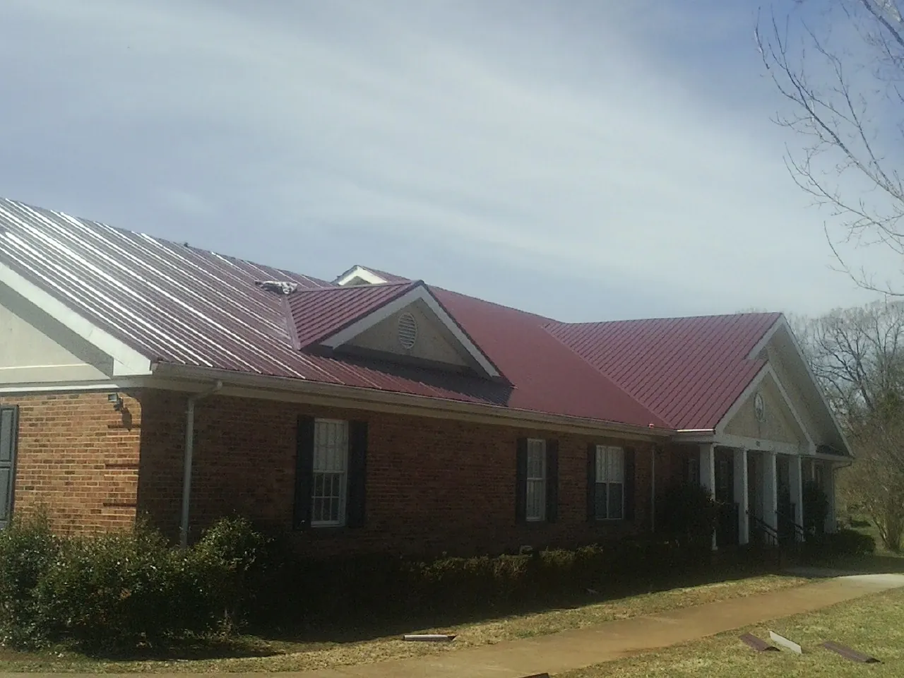 Red metal roof with gabled entries on a long brick building, from a Hail Damage Roof Repair job in Grandville