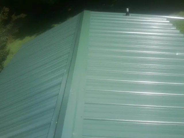 New green metal panels meeting at the ridge of a roof — Flat Roof Repair work by our crew in Grandville