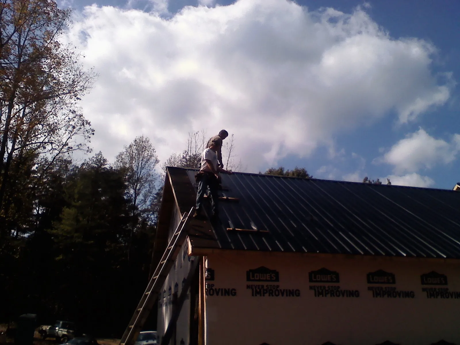 Roofer fastening dark metal panels high against a cloudy sky, from a Roof Inspection job in Grandville