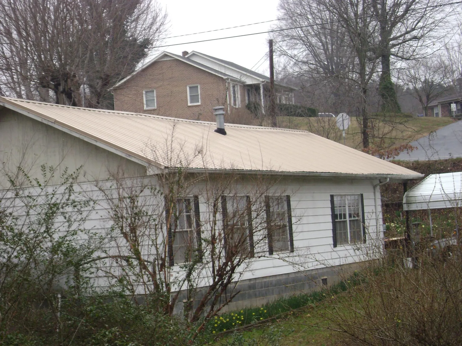 Tan metal roof on a white sided house set into a hillside — Commercial Roofing by Roofing Brothers in Grandville