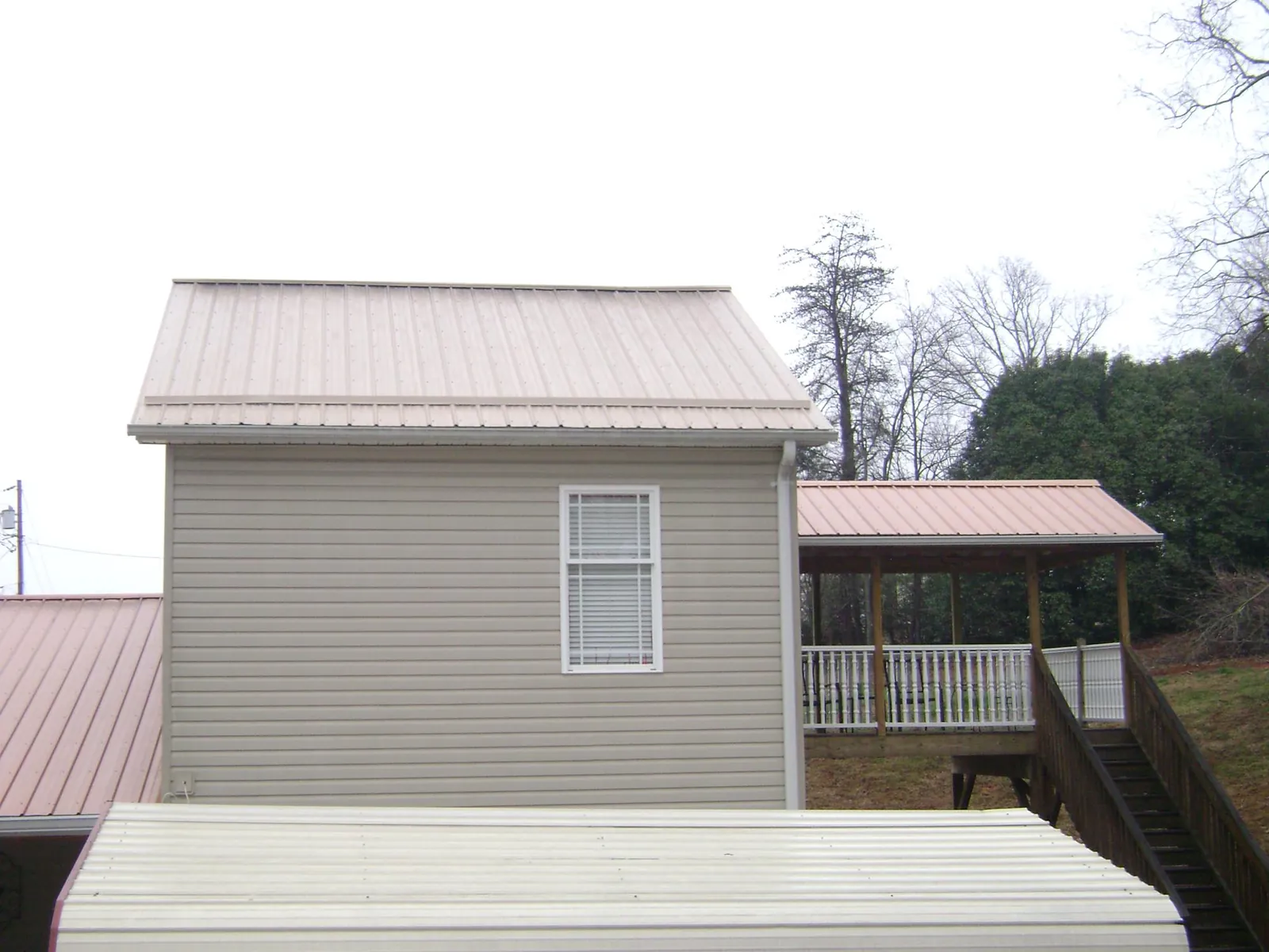 Tan metal roofs on a two story addition and attached porch, from a Roof Replacement job in Grandville